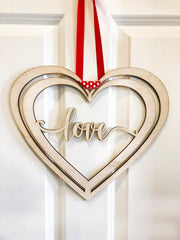 Heart-shaped mirror with 'love' text and red ribbon on a white door