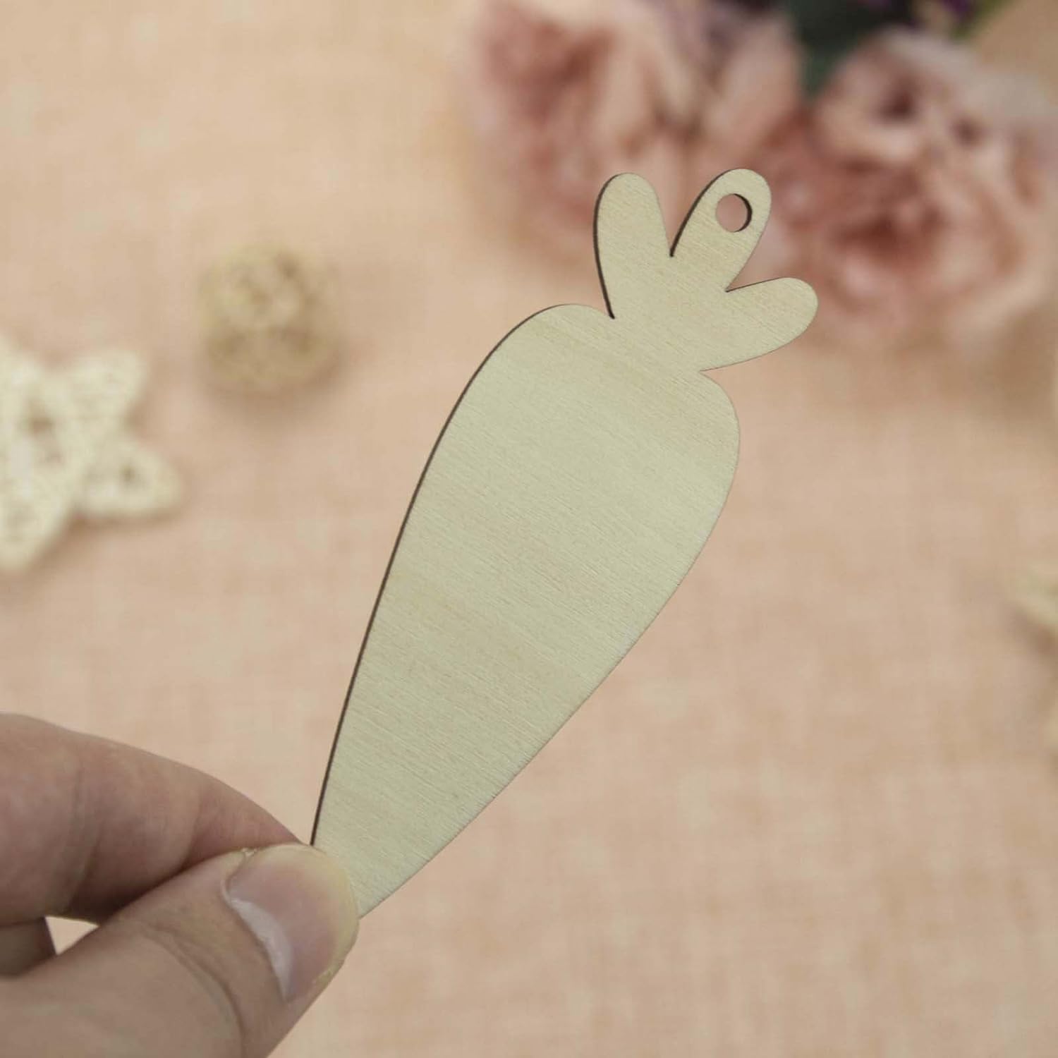Hand holding a beige carrot-shaped cutout against a blurred floral background