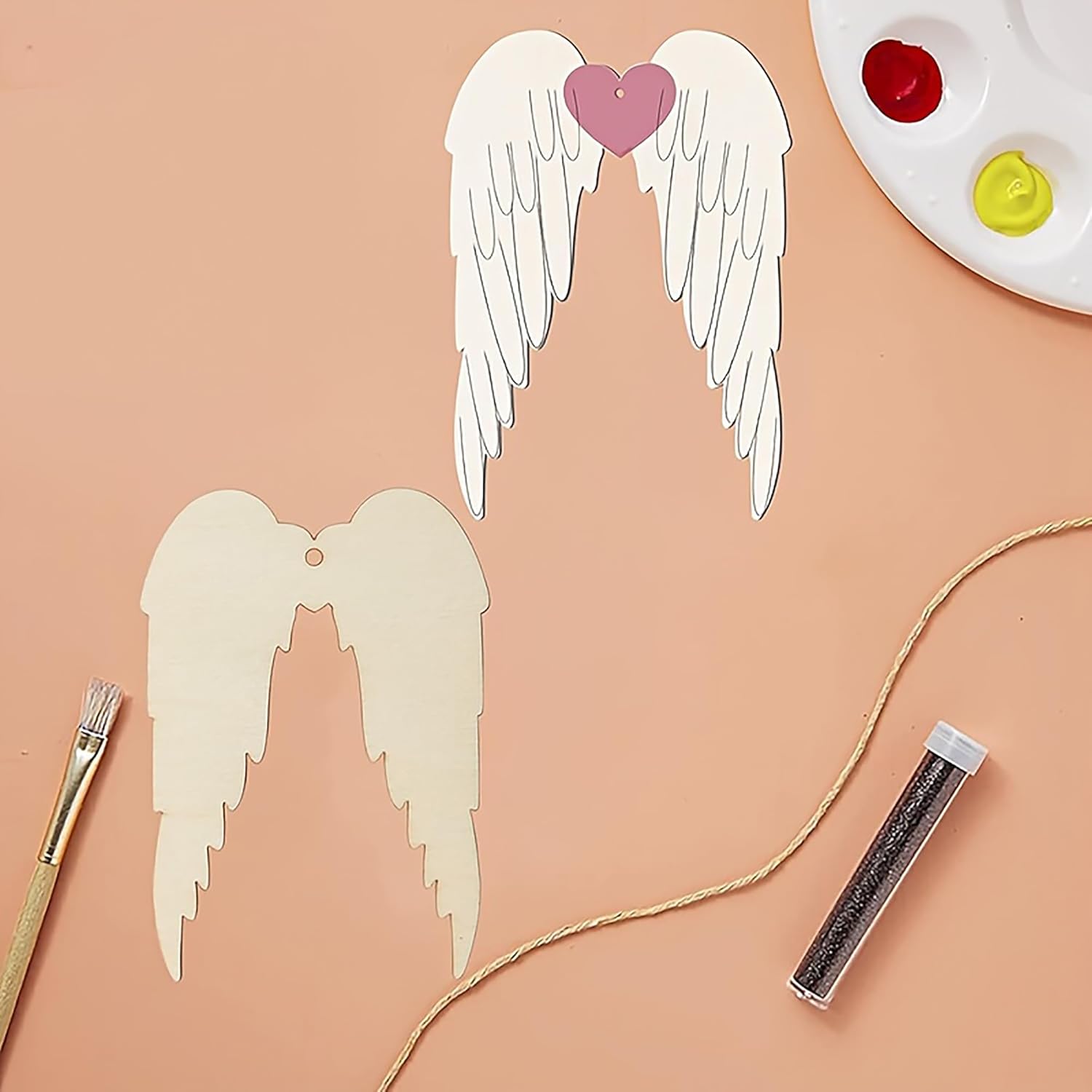 Cardboard angel wings with a heart, paintbrush, and glitter on a peach background