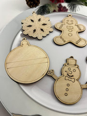 Wooden Christmas ornaments including a snowflake, gingerbread man, ball, and snowman on a white plate.