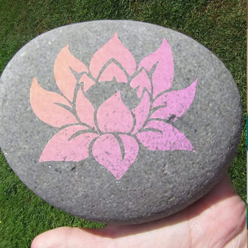 Decorative stone with a pink lotus flower design held by a hand on grass.