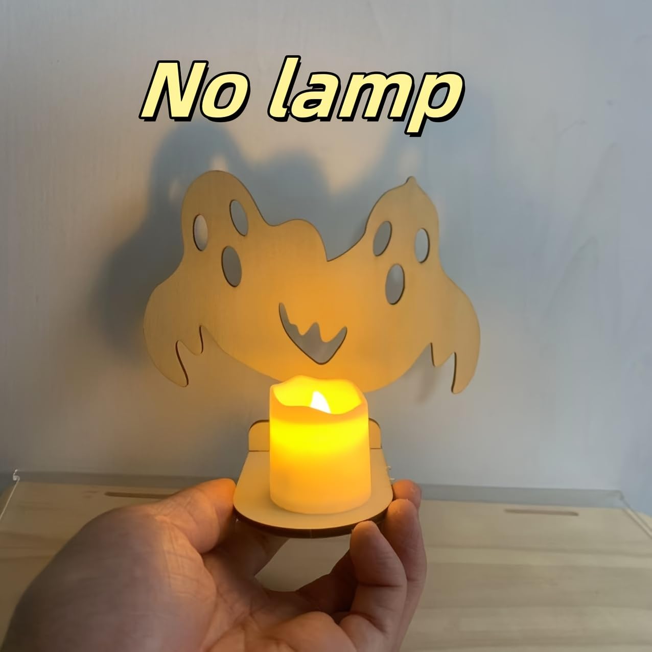 Hand holding a small lamp with a ghost design on a plain background