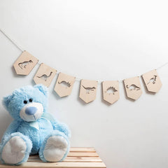 Blue teddy bear next to a wooden banner with dinosaur shapes on a light gray background