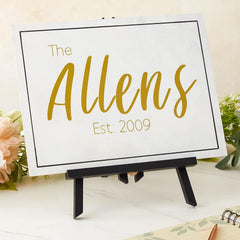 Personalized sign with 'The Allens Est. 2009' on a stand with flowers in the background