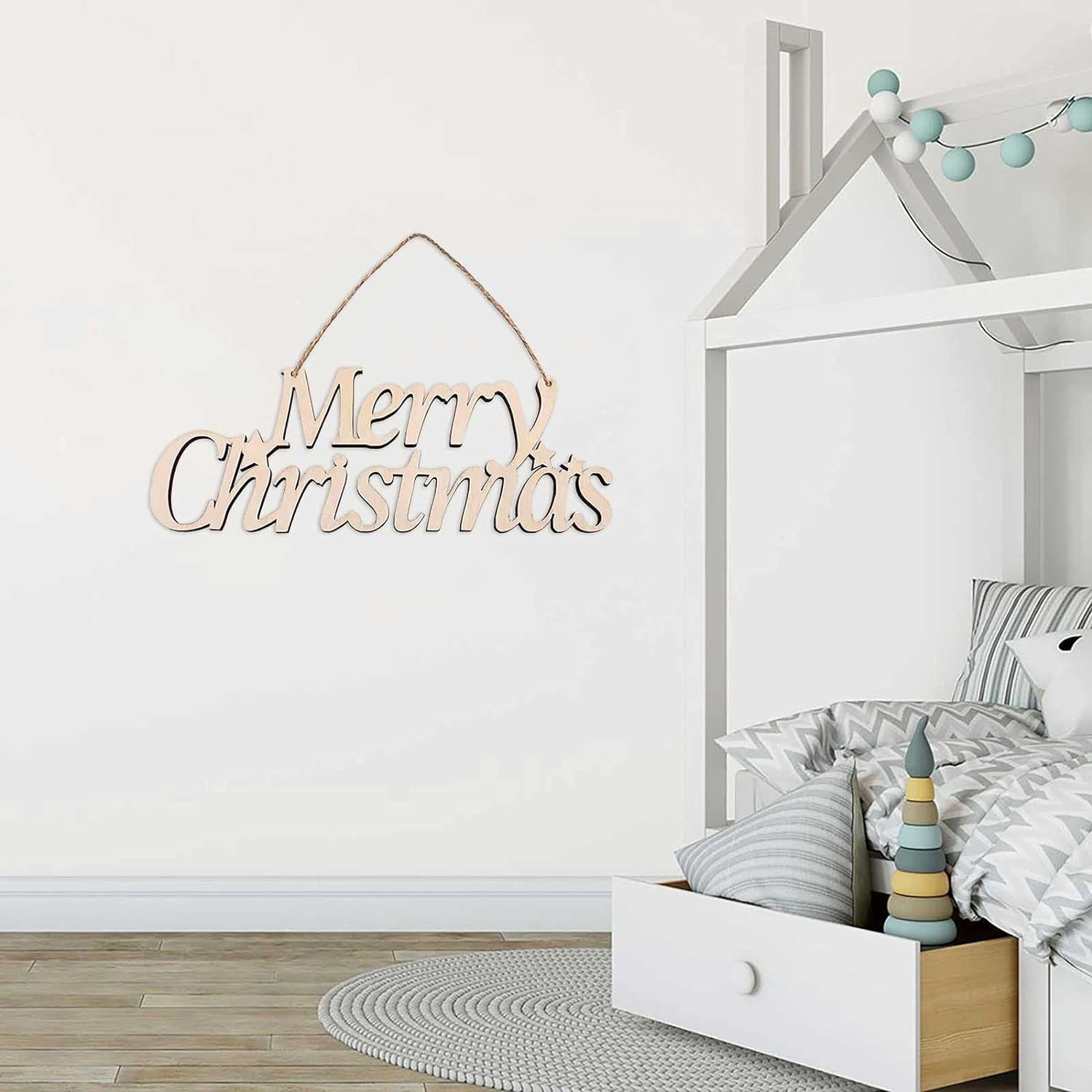 Wooden 'Merry Christmas' decoration on a wall in a child's bedroom with a bed and toys.