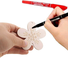 Hand holding a small pink flower-shaped object with another hand using a black marker to draw on it, with a red marker in the background.
