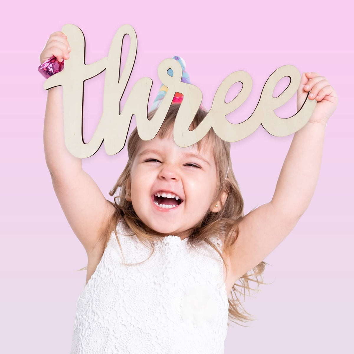 Child holding up the word 'three' against a pink background