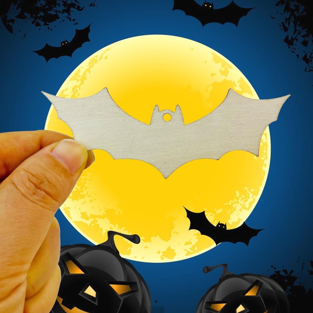 Hand holding a bat-shaped object with pumpkins and bats against a moonlit sky