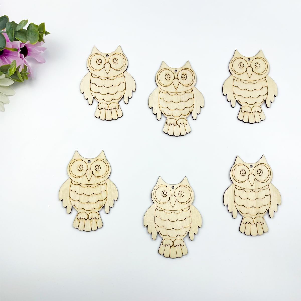 Six wooden owl ornaments on a white background with a small bouquet of flowers.