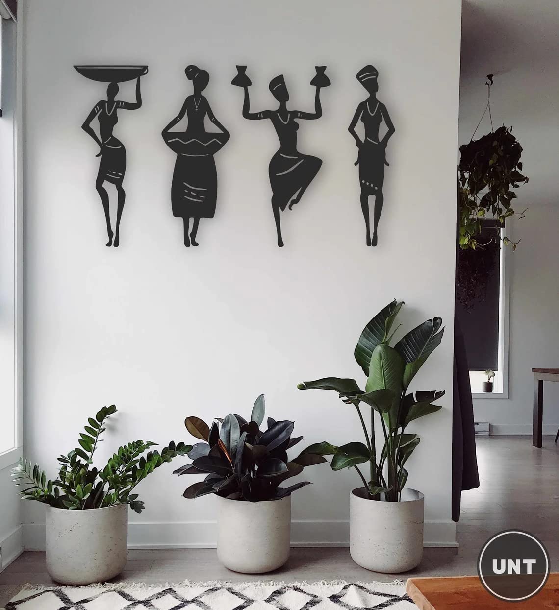 Decorative wall art of black silhouettes on a white wall with potted plants below.