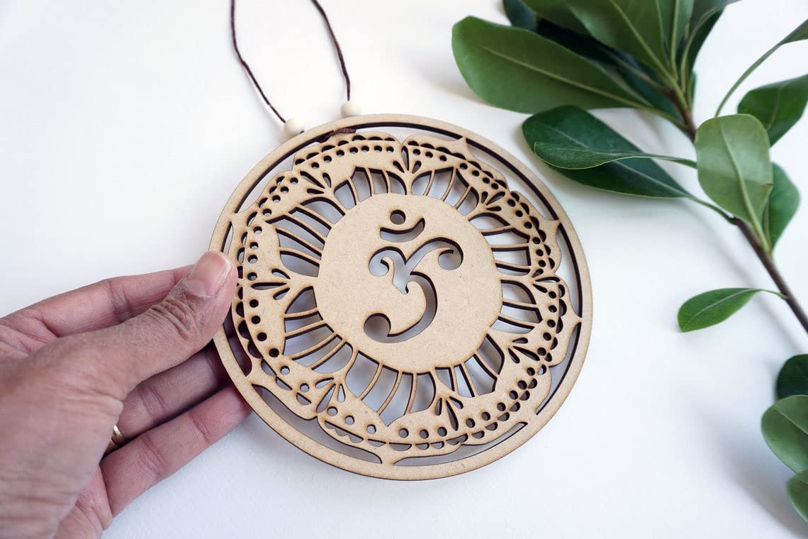 Wooden ornament with Om symbol held by a hand on a white background with green leaves.