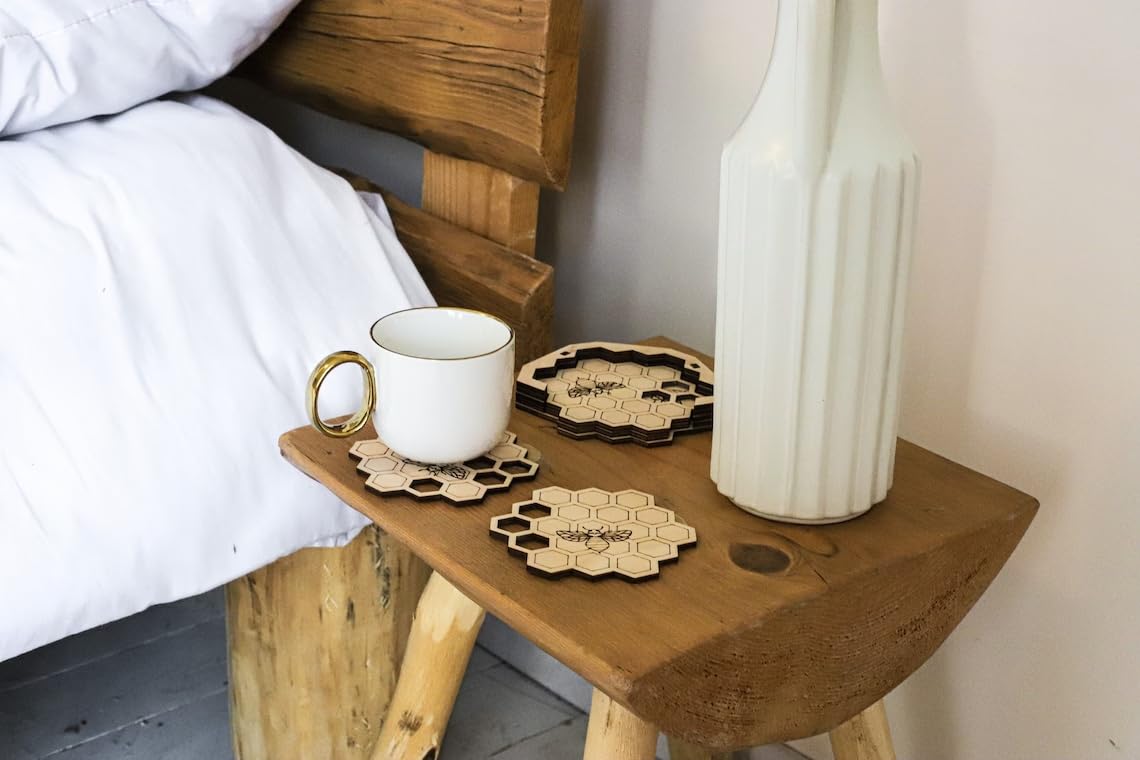 Wooden side table with a mug, coasters, and a vase next to a bed.