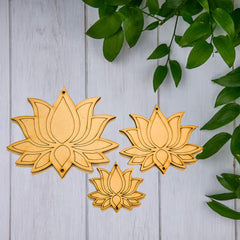 Three wooden lotus flower ornaments on a light wooden background with green leaves.