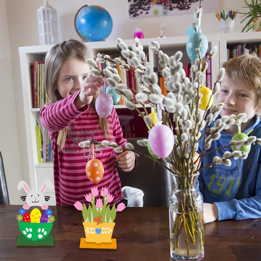 Two children decorating pussy willow branches with Easter eggs and bunnies in a home setting.