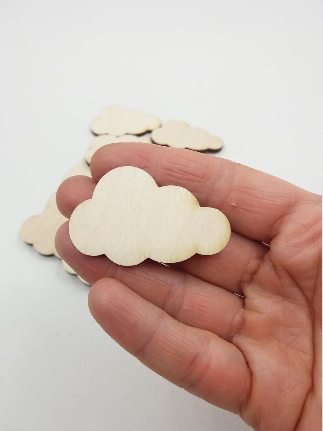 Wooden cloud-shaped cutouts held in a hand against a white background