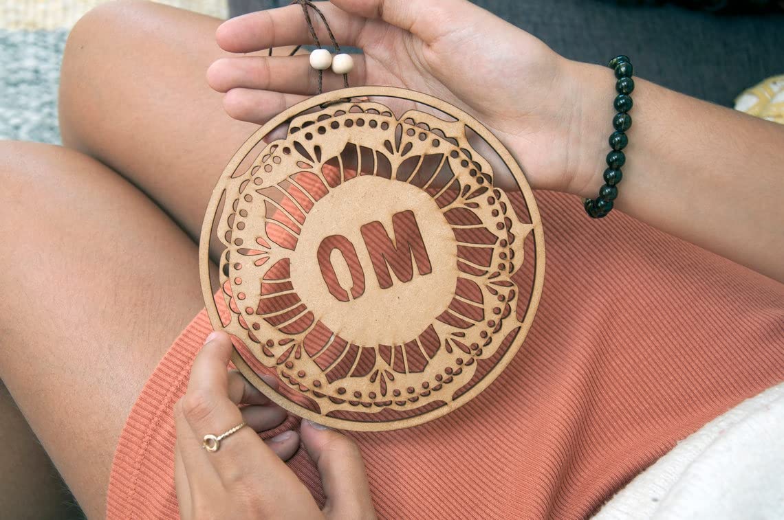 Person holding a wooden disc with 'OM' engraving on a soft surface