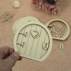 Wooden fairy door with heart design held by a hand on a textured surface with decorative elements.