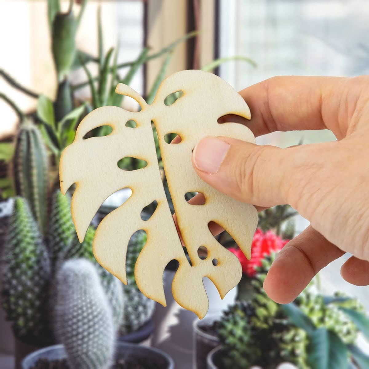 Hand holding a wooden leaf-shaped ornament with plants in the background
