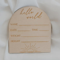 Wooden baby milestone card with 'hello world' text and blank lines for personalization on a white background.