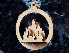 Wooden Christmas ornament with cut-out design of a snowy landscape and trees against a dark background.