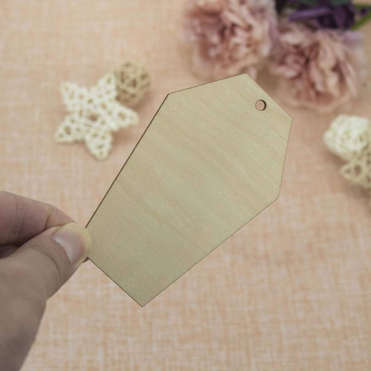 Hexagonal wooden tag held by a hand with a floral background