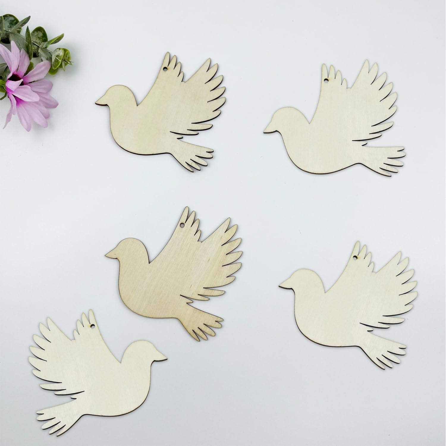 Five wooden dove shapes on a light background with a pink flower.