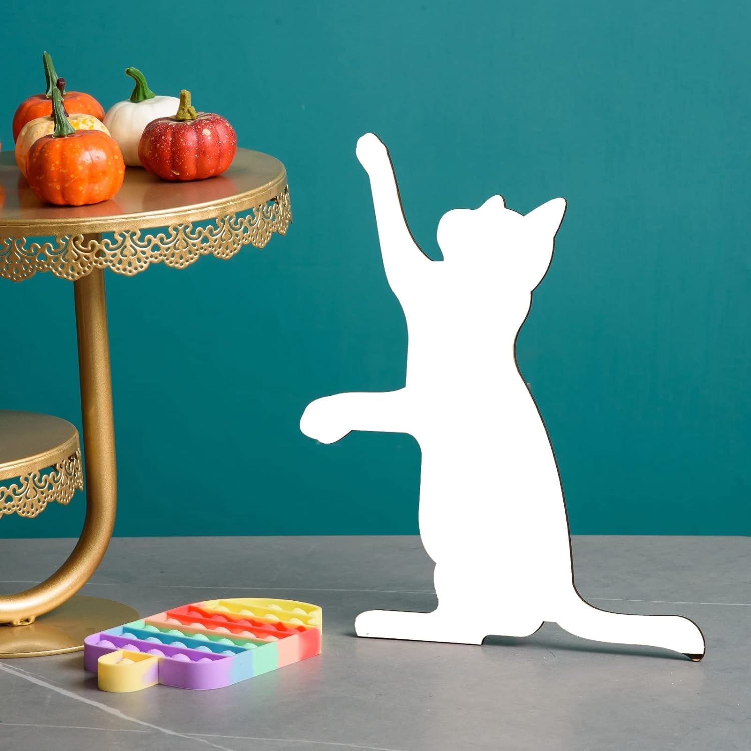 White cat-shaped stand on a gray surface with colorful toys and pumpkins in the background.