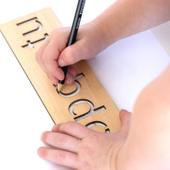 Child's hand writing on a wooden alphabet board with a pen.