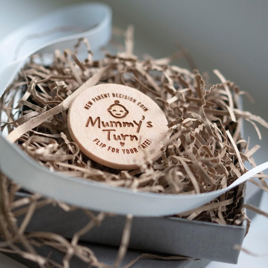 Wooden coin with 'Mummy's Turn' text on a bed of straw in a box.
