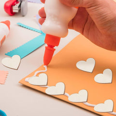 Hand applying glue to a piece of paper with heart shapes on a light background