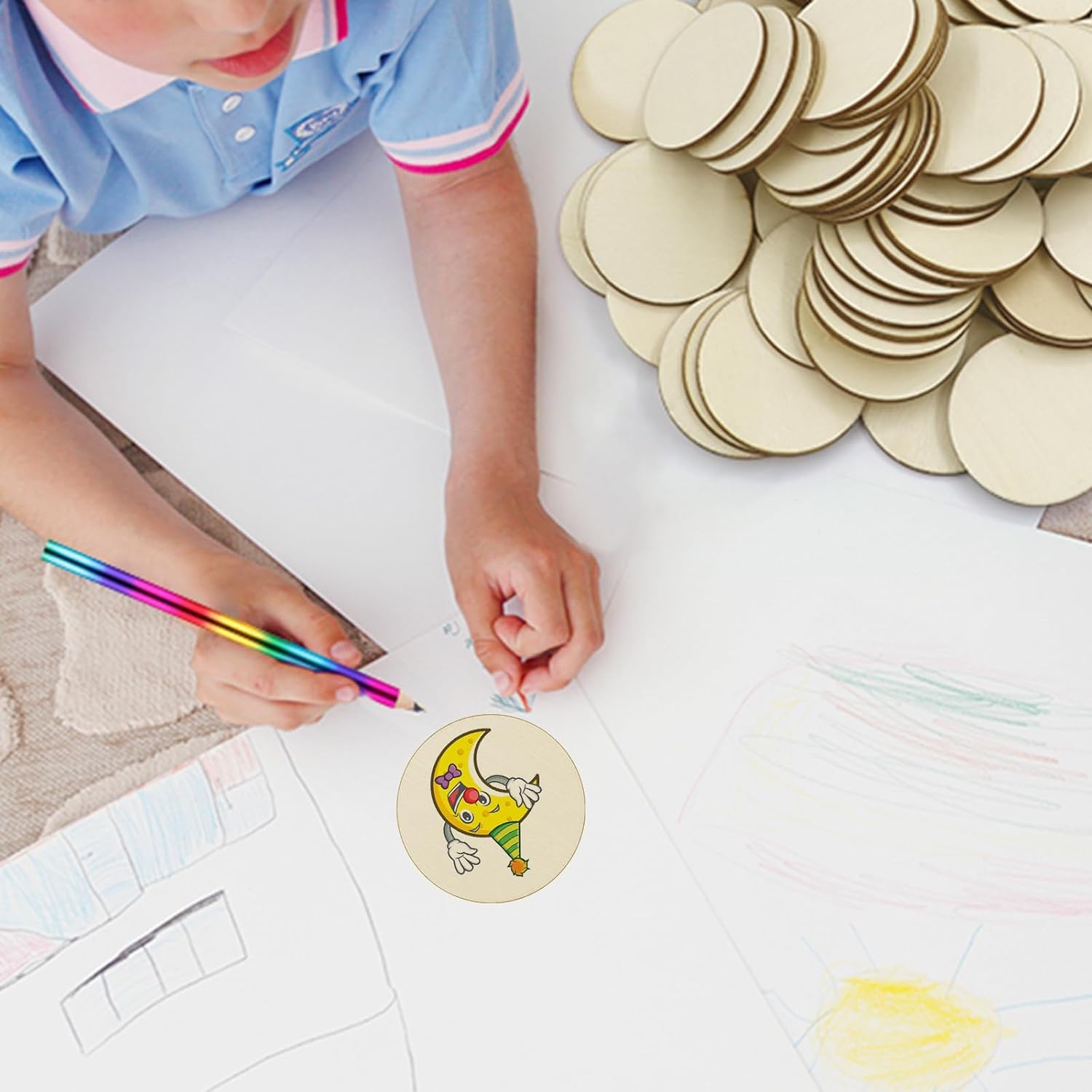Child coloring a circular craft item with a rainbow pencil, surrounded by more circular crafts on a white surface.