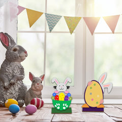 Decorative Easter items including a rabbit figurine, colorful eggs, and bunny-shaped cards on a table with a window and bunting in the background.