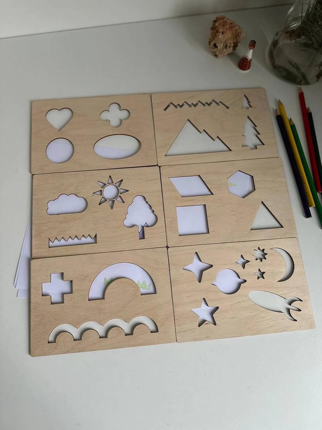 Wooden shape sorting puzzle on a white surface with pencils and a small figurine.