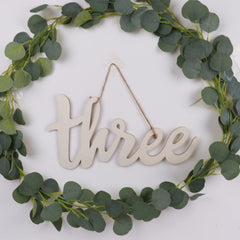 Decorative wreath with green leaves and a wooden 'three' sign on a white background
