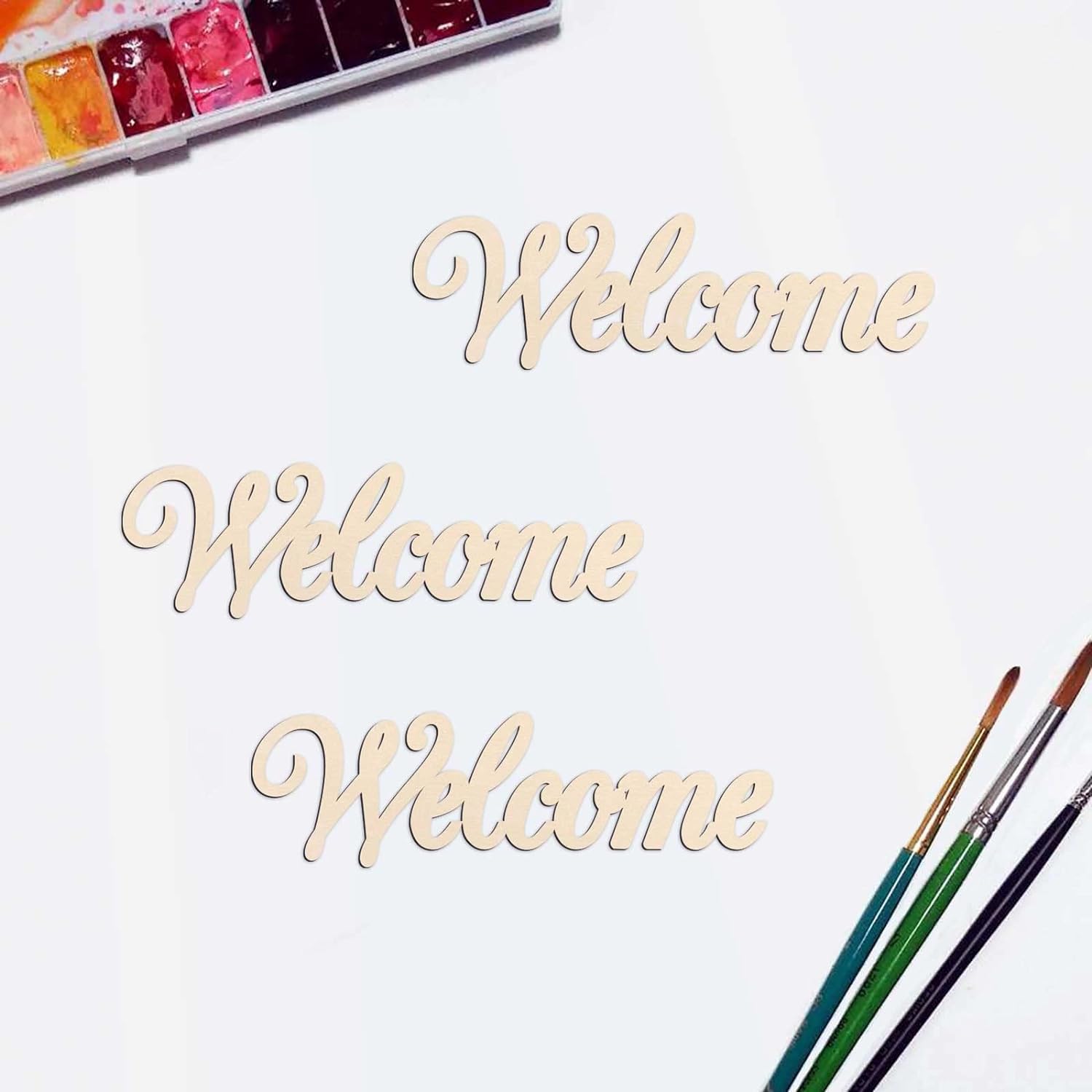 Wooden 'Welcome' sign with watercolor paint set and brushes on a white background