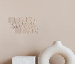 Decorative wall art with 'Home Sweet Home' on a beige wall with a white vase and cube below.