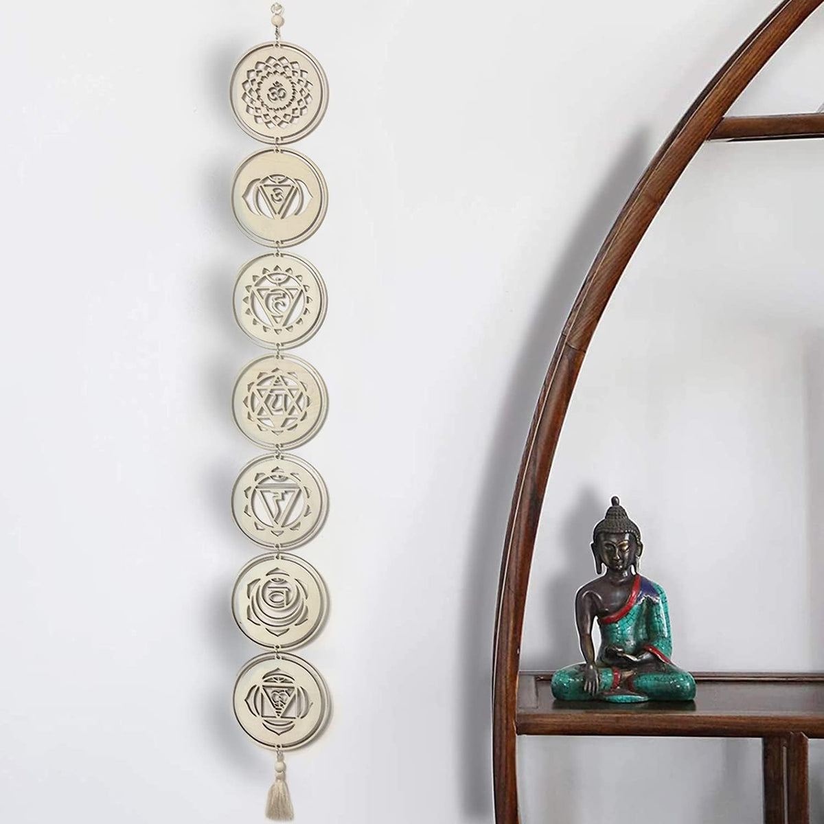 Decorative wall hanging with chakra symbols next to a Buddha statue on a wooden shelf.