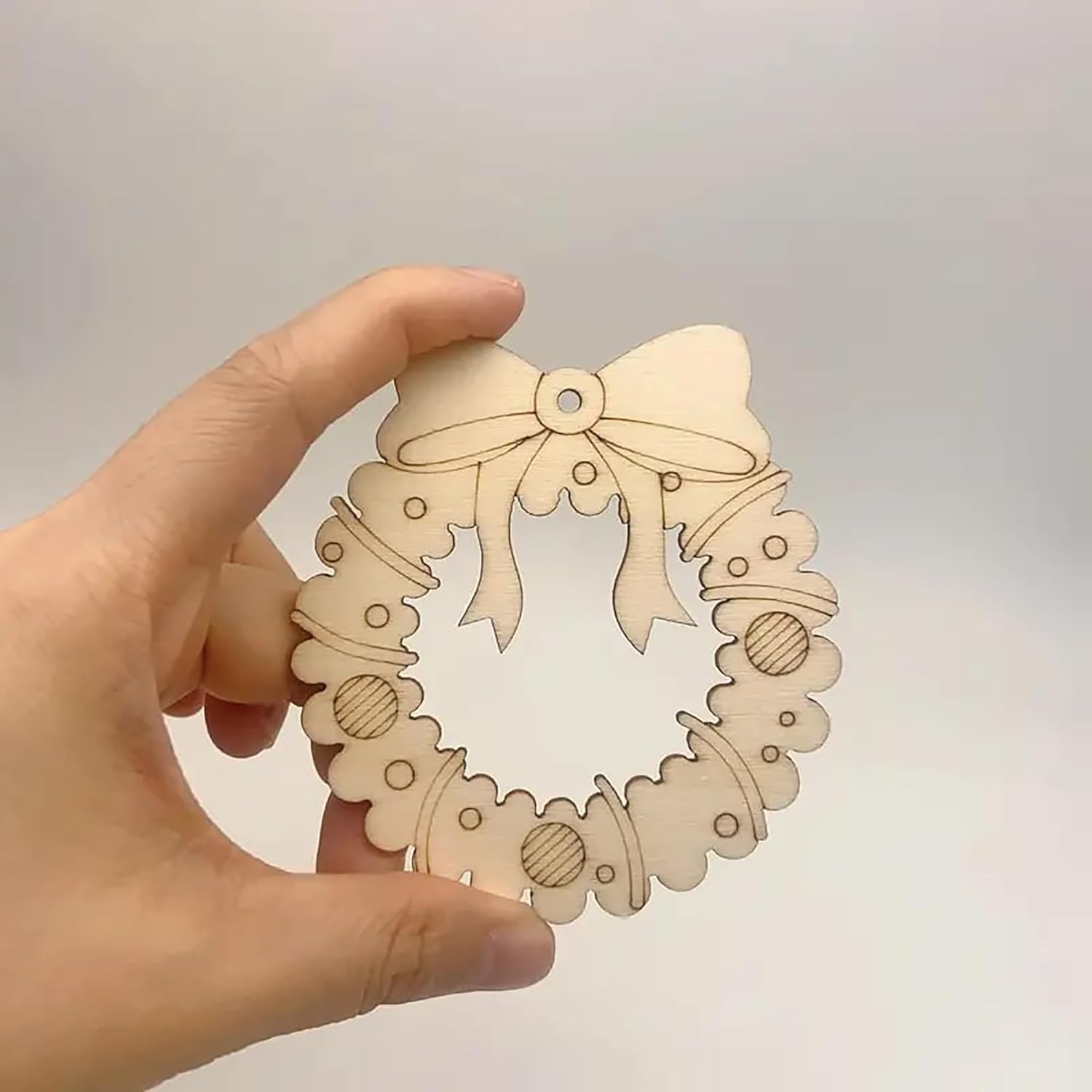 Hand holding a wooden Christmas wreath ornament with a bow on a light gray background