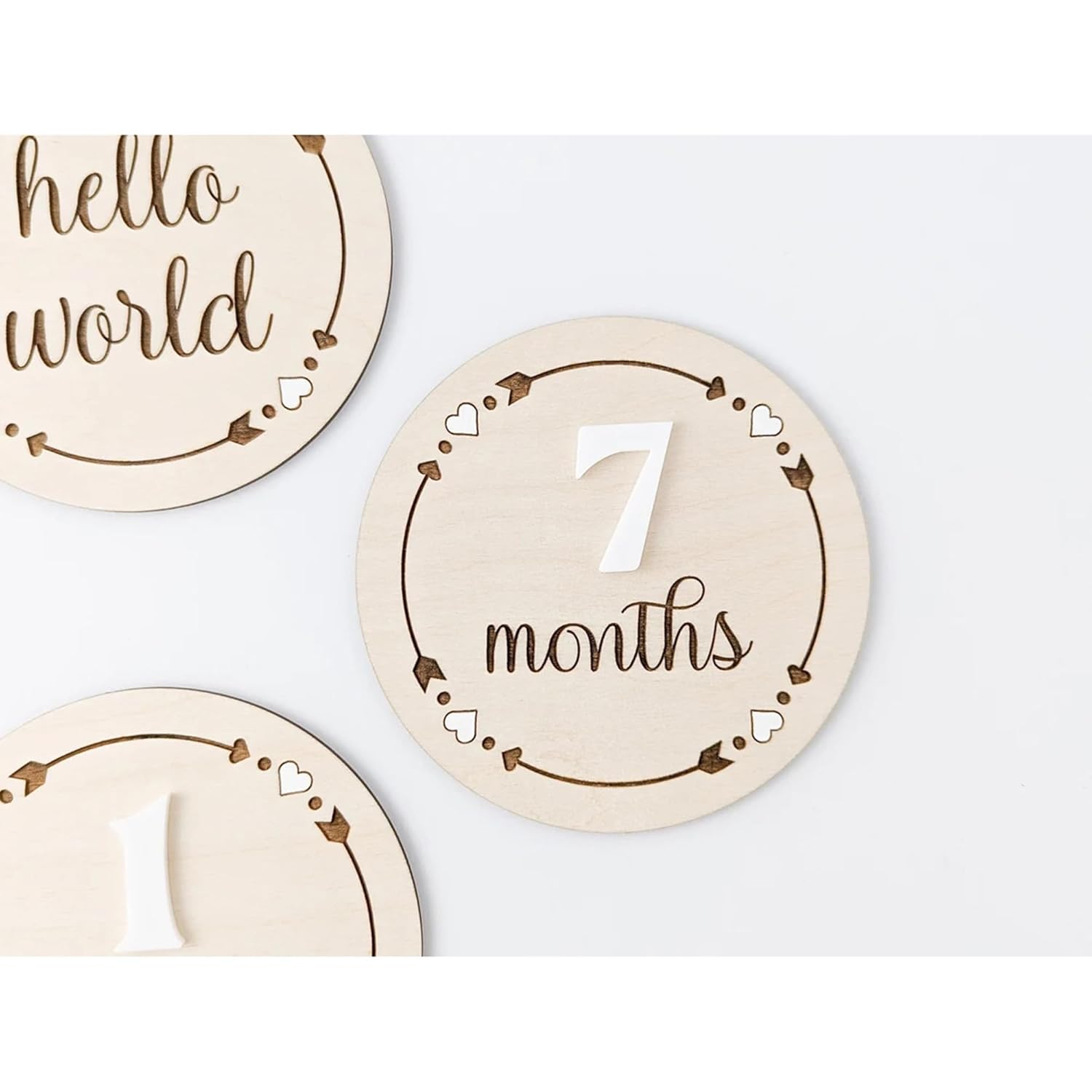 Wooden milestone discs with 'hello world' and '7 months' text on a white background