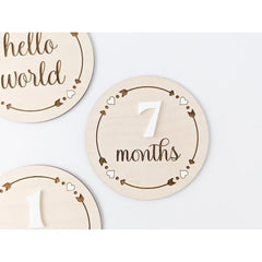 Wooden milestone discs with 'hello world' and '7 months' text on a white background