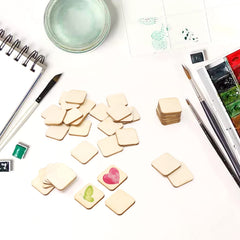 Small square tiles with colorful designs on a white surface with art supplies.
