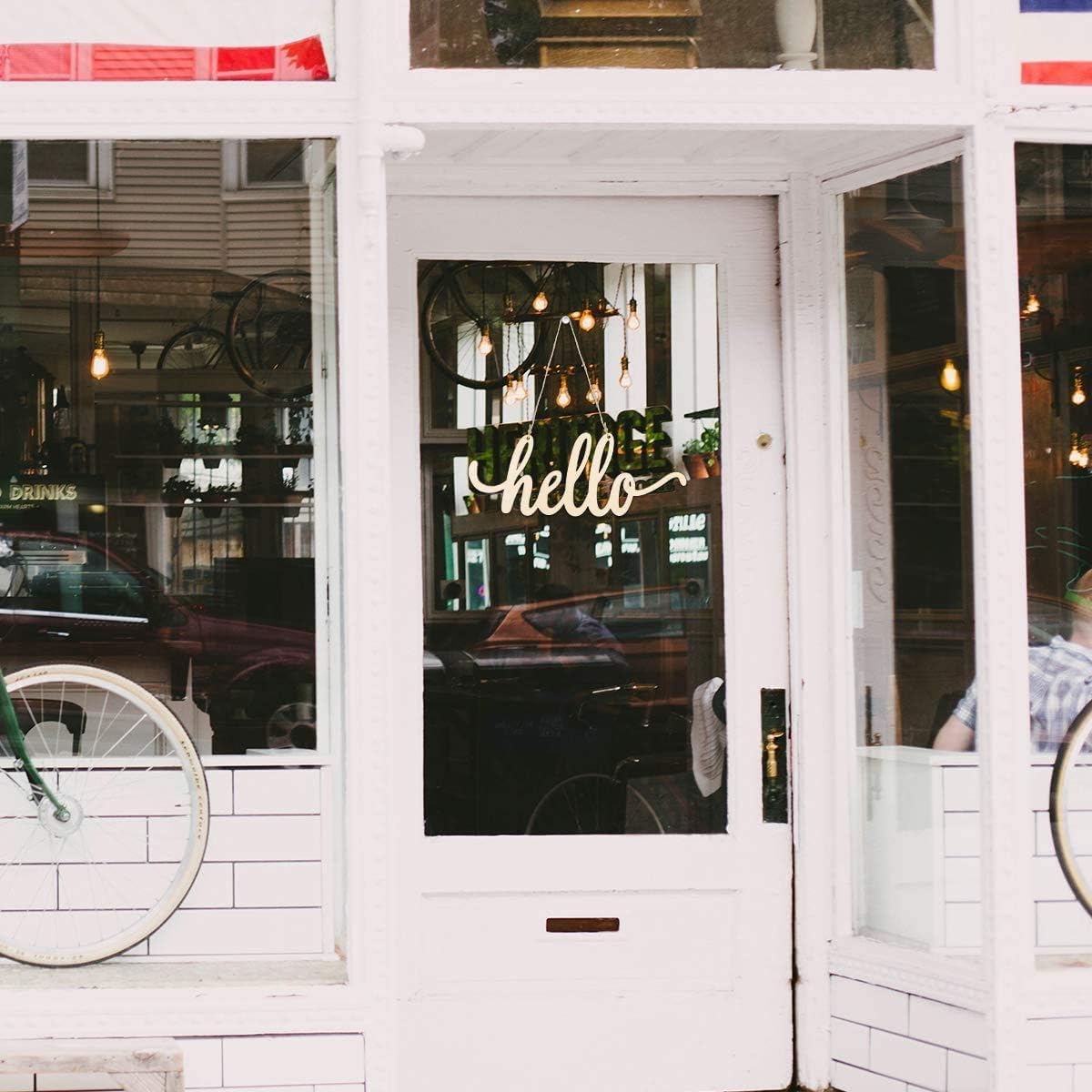 Storefront with a 'hello' sign on the glass door, surrounded by bicycles and a white wall.
