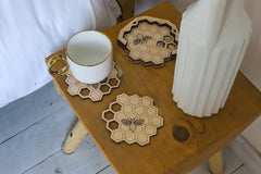 Hexagonal coasters with bee design on a wooden table with a mug and vase.
