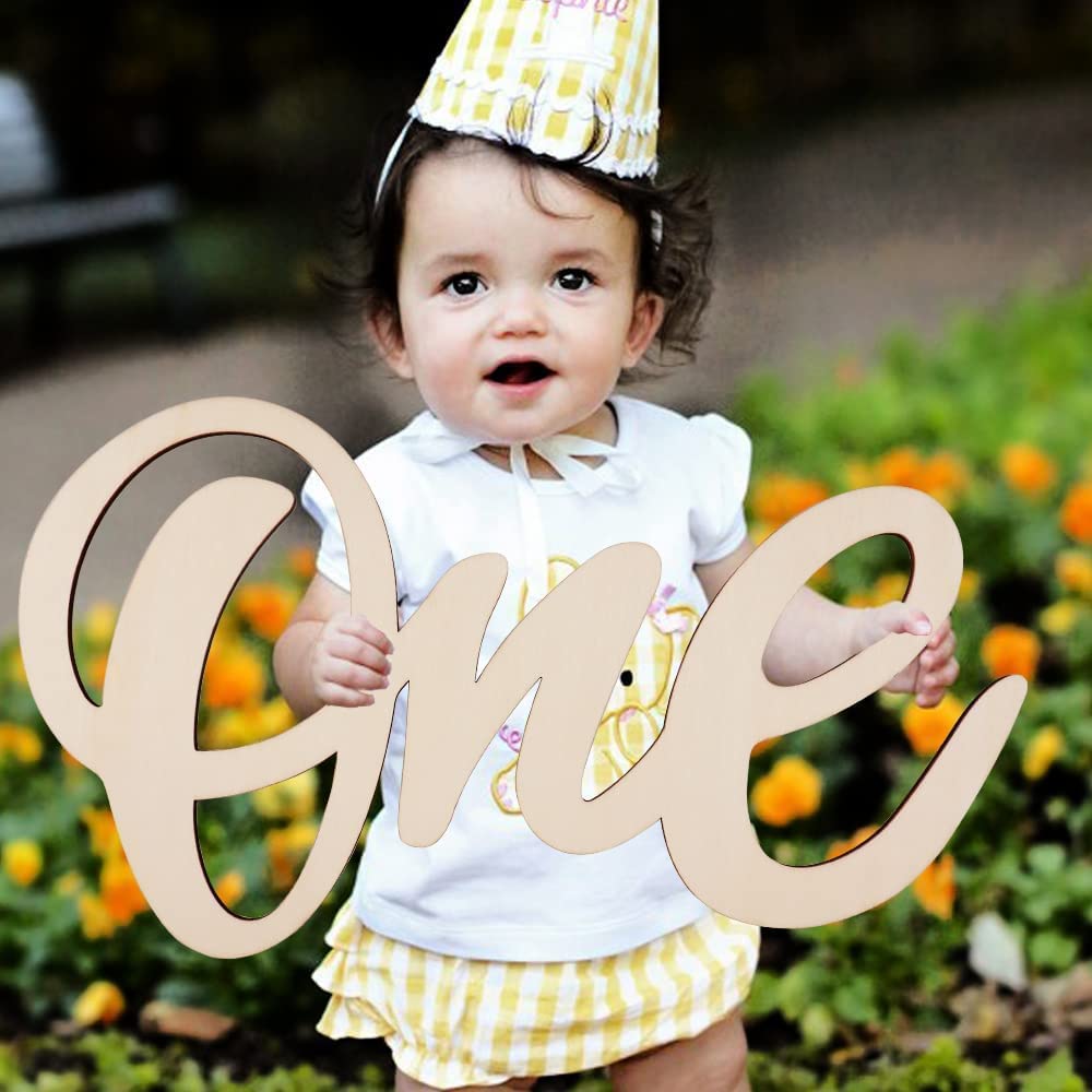 Child celebrating a first birthday with a 'one' sign outdoors.