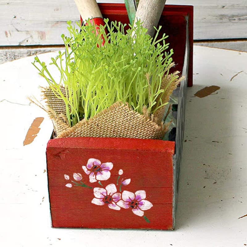 Red wooden planter with floral design containing green plants on a white surface.