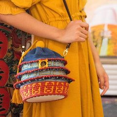 Person wearing a yellow dress holding a colorful woven bag with intricate patterns.