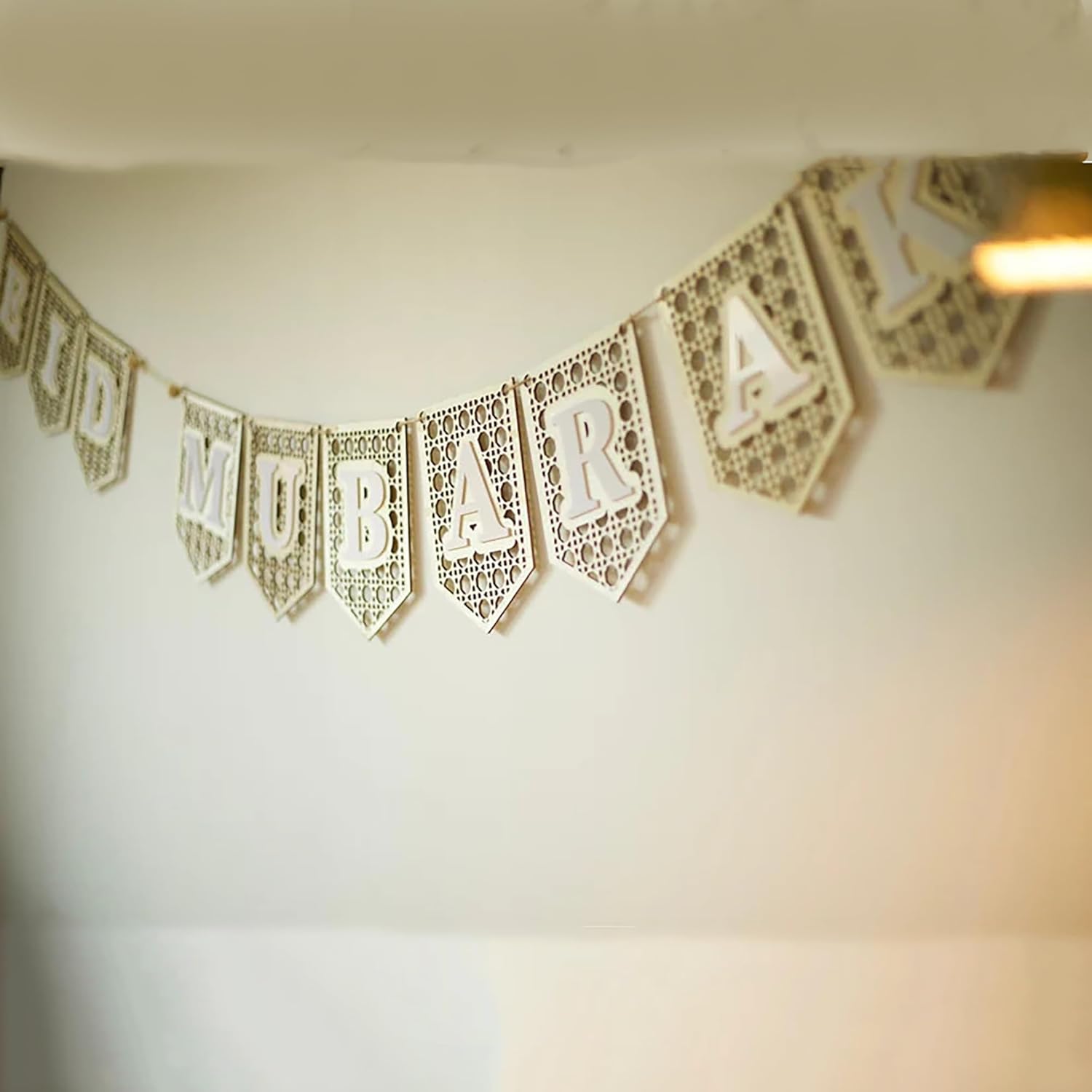 Decorative banner with cut-out letters spelling 'MUBARAK' on a plain background.