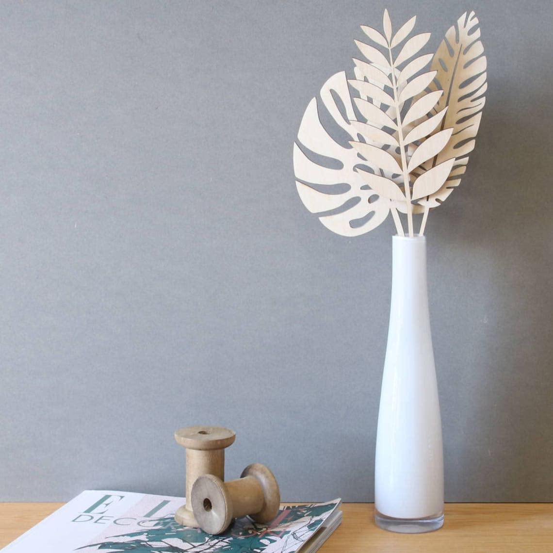 White vase with leaf-shaped object on a wooden surface against a gray wall