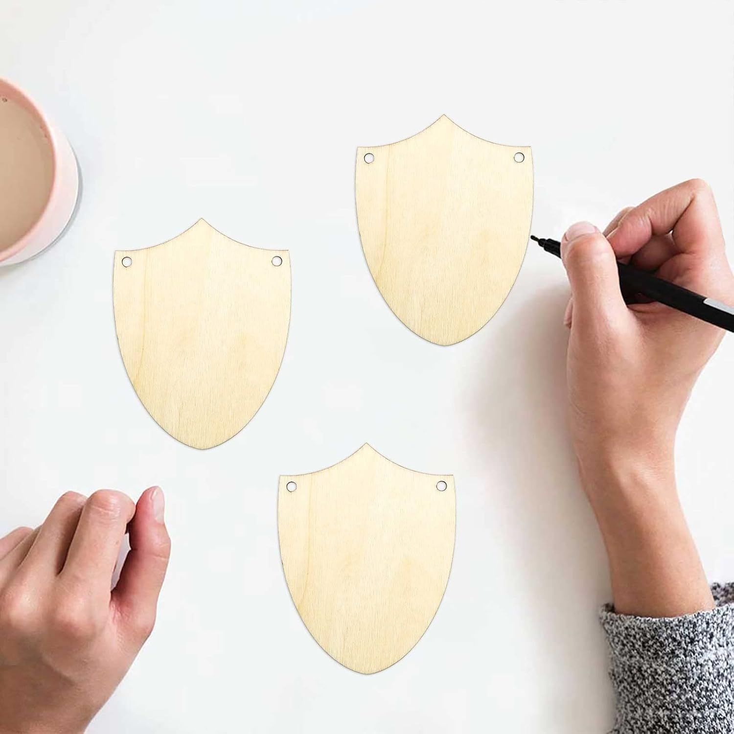 Shield-shaped wooden cutouts with a hand using a marker on a white background