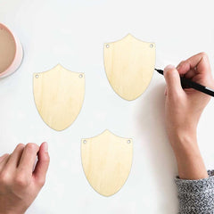Shield-shaped wooden cutouts with a hand using a marker on a white background